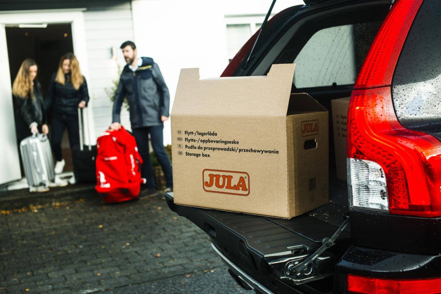 Flyttekasse i en bil med tre mennesker stående længere væk
